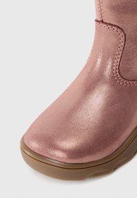 Vaaleanpunaiset metallinhohtoiset nilkkurit, joissa on sileä pintarakente, pyöreä kärki ja kumipohja. Sivuille ja kantapäähän on ommeltu koristeelliset yksityiskohdat.