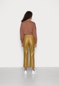 Un pull marron surdimensionné, un pantalon large en simili cuir jaune et des baskets blanches. La tenue présente une coupe décontractée et des textures douces.