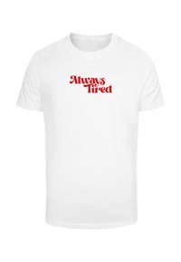 Bílý bavlněný tričko s kulatým výstřihem; obsahuje frázi "Vždy unavený" v tučném červeném retro písmu. Krátké rukávy, jednoduchý design.