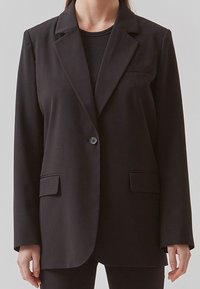 Blazer nero in tessuto liscio, con un bottone singolo, rever con asola e due tasche frontali. Vestibilità sartoriale e maniche lunghe.