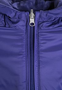 Fialová zipová bunda s hladkým, lesklým materiálem, YKK zipem a měkkou podšívkou. Límec se nastavuje pro větší teplo.