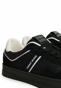Czarno-białe sneakersy Tommy Jeans z zamszowymi i siateczkowymi teksturami, czarną podeszwą oraz logo marki po boku i na języku.