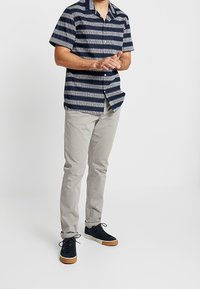 Tričko s krátkými rukávy s námořnicky modrými a bílými vodorovnými pruhy; doplněné světle šedými kalhotami a tmavými teniskami s hnědými podrážkami.