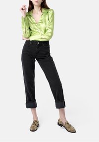 Green satin button-up shirt, black tapered jeans, and snake-print slip-on shoes. The shirt has a wide collar; jeans are cuffed at the ankles.