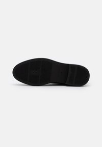 Suela de zapato de goma negra con una superficie texturizada, que presenta patrones rectangulares y agarres elevados para tracción.