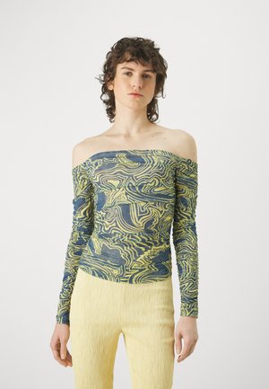 Off-shoulder lange mouwen top in blauw en geel spiraalpatroon, met textuurstof; gecombineerd met lichtgele flared broeken.