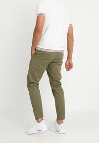 Gröna bomullschino byxor med tapered passform, framfickor och elastiska muddar. Bärs med en vit ribbad kortärmad skjorta och vita sneakers.