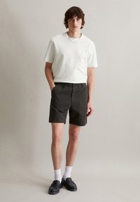 Witte korte mouwen t-shirt, zwarte shorts met elastische tailleband, gestructureerde stof, gecombineerd met witte sokken en zwarte instap schoenen. Eenvoudig ontwerp.