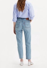 Ljusblå högmidjade jeans med raka ben, blekt tvätt, och signatur bakfickor, matchat med en blå-randig blus och silverfärgade skor.