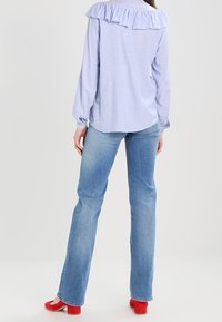 Hellblause gestreifte Bluse mit Rüschensaum, kombiniert mit mittelblauen Schlagjeans und roten High Heels. Glatte Texturen und lässiges Design.