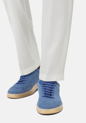 Zapatillas de ante azul con cordones azules, suela de goma y detalles perforados. Combinadas con pantalones blancos ligeramente recortados.