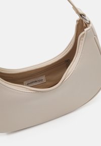 Bežová kabelka ve tvaru půlměsíce se zipovým uzávěrem a vnitřní kapsou na zip, uvnitř je vidět textilní štítek.