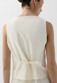 Ivory mouwloze top met een textuurstof, recht gesneden, met een strikdetail op de rug en subtiele naden, wat zorgt voor een getailleerde silhouet.