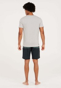 Grijze t-shirt met korte mouwen en geribbelde halslijn, gecombineerd met donkere shorts met een horizontaal gestreepte tailleband, zonder schoenen.