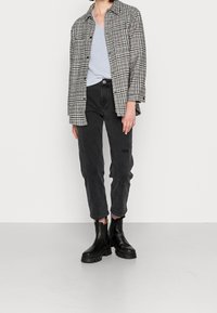 Veste à carreaux grise et noire, débardeur en dentelle bleu clair, jean noir fuselé et bottines noires à semelles épaisses.
