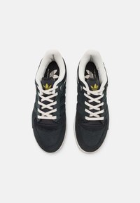 Tumši zaļi treniņi ar baltām auklām un teksturētu augšpusi. Iespējas ietver svītru rakstu uz mēles un perforētus elementus uz pirksta.