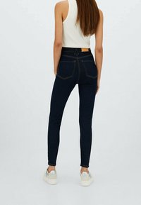 Mörkblå skinny jeans i denim med hög midja, med bakfickor och subtila sömdetaljer, i kombination med ljusa sneakers.