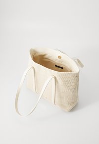 Vævet creme tote taske med et herringbone-mønster, hvide syntetiske håndtag og en indvendig lynlåslomme. Lukning med en trykknap.