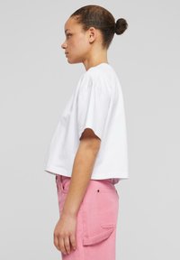 Tricou scurt alb cu mâneci scurte, asortat cu pantaloni roz deschis, prevăzuți cu buzunare laterale și un design drept.