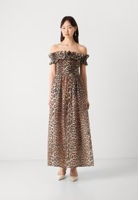 Maxikleid mit Leopardenmuster, das einen gerafften Oberkörper, schulterfreie Rüschensäume und durchsichtigen Stoff aufweist. Abgerundet mit beigen Schuhen.