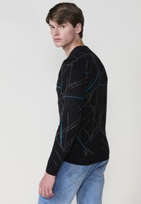 Suéter negro con patrones abstractos en gris y azul, escote redondo, mangas largas, diseño ajustado, y dobladillo y puños acanalados, combinado con jeans claros.