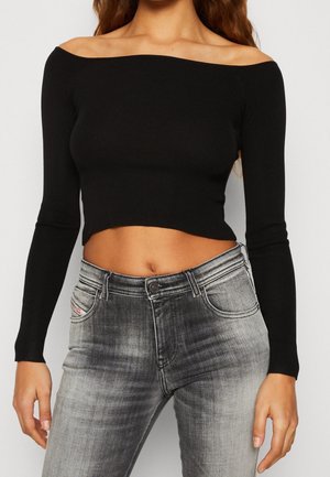 Femme portant un haut court noir à manches longues et épaules dénudées, associé à un jean gris délavé taille haute.
