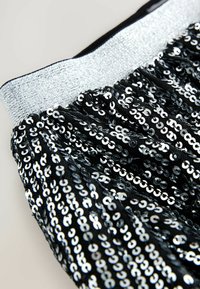 Jupe noire avec des sequins et une ceinture en argent. Les sequins créent un motif texturé, réfléchissant la lumière avec une finition brillante.
