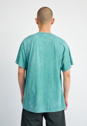 T-shirt en coton turquoise avec une coupe décontractée, manches courtes, col rond et texture délavée. Caractérisé par un ourlet droit et des détails minimalistes.