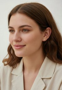 Boucles d'oreilles en forme de fleur en or, avec cinq pétales délicats et une finition lisse, portées par un mannequin aux cheveux ondulés de couleur brun moyen.