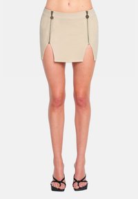 Mini gonna beige con zip laterali, design aderente, texture liscia, vita alta e aperture a spacco per una silhouette moderna e slanciata.