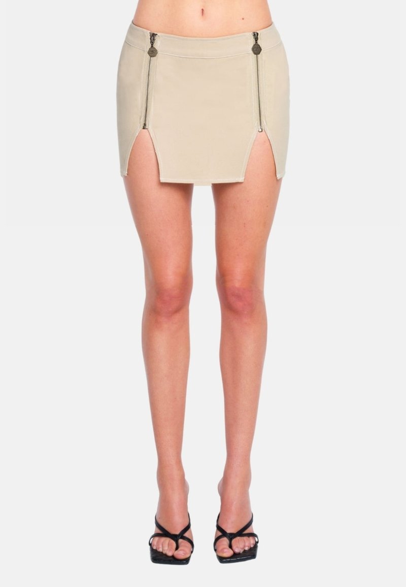 Mini gonna beige con zip laterali, design aderente, texture liscia, vita alta e aperture a spacco per una silhouette moderna e slanciata.