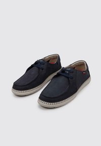 Chaussures en daim bleu marine avec un laçage et une couture beige contrastante ; texture lisse et forme de bout rond.