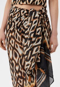 Wickelrock mit einem auffälligen Tierdruckmuster in Braun, Schwarz und Creme, aus leichtem Stoff mit Quastenakzenten und einem geknoteten Band.