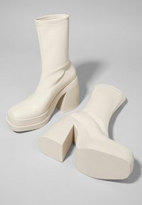 Kermaväriset muotikengät nilkkamalleilla, joissa on sileä pinta, pyöreä kärki ja lohkokorko. Sisältää korkean, elastisen siluetin ja ompeluyksityiskohtia.