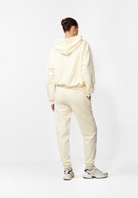 Kremowy zestaw składający się z bluzy i spodni dresowych, z kapturem, luźnym krojem i żebrowanymi mankietami. Tkanina wydaje się być miękka i teksturowana.