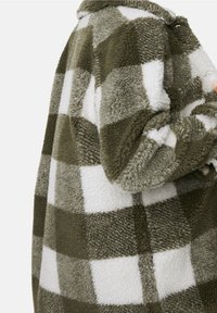 Chaqueta de cuadros verde y blanca hecha de suave forro polar texturizado. Presenta grandes patrones de cuadros y detalle de botones en la parte delantera.