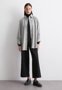 Chemise à rayures noir et blanc, associée à un pantalon large noir et des chaussures à enfiler noires. Tissu doux, coupe décontractée.