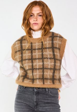 Gilet lavorato a maglia beige con un motivo a quadretti marroni e crema, caratterizzato da un collo rotondo e senza maniche, abbinato a jeans scuri.