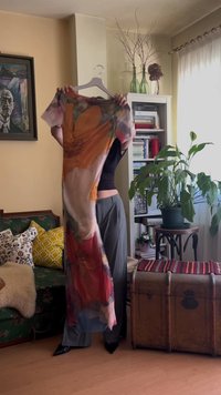 Durchsichtiges, fließendes Kleid mit einem mehrfarbigen Blumenmuster in Orange-, Pink- und Rottönen. An einem Kleiderbügel präsentiert, mit kurzen Ärmeln und einem lockeren Schnitt.