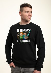 Felpa nera con grafica pixelata "Buon Compleanno", con personaggi e armi, posizionata su uno sfondo a contrasto.