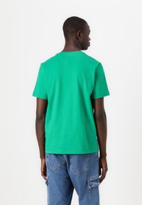 T-shirt en coton vert à manches courtes et col rond, avec un subtil détail de couture en forme de V à l'arrière.