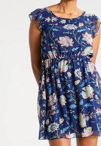 Námořnické modré květinové šaty s krátkými volánovými rukávy, elastickým pasem a splývavou sukní s barevnými květinovými vzory v růžové a zelené barvě.