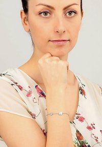 Bracciale in argento con ciondoli a forma di cuore e gatto. Il modello indossa una blusa a fiori realizzata in un tessuto morbido e trasparente.