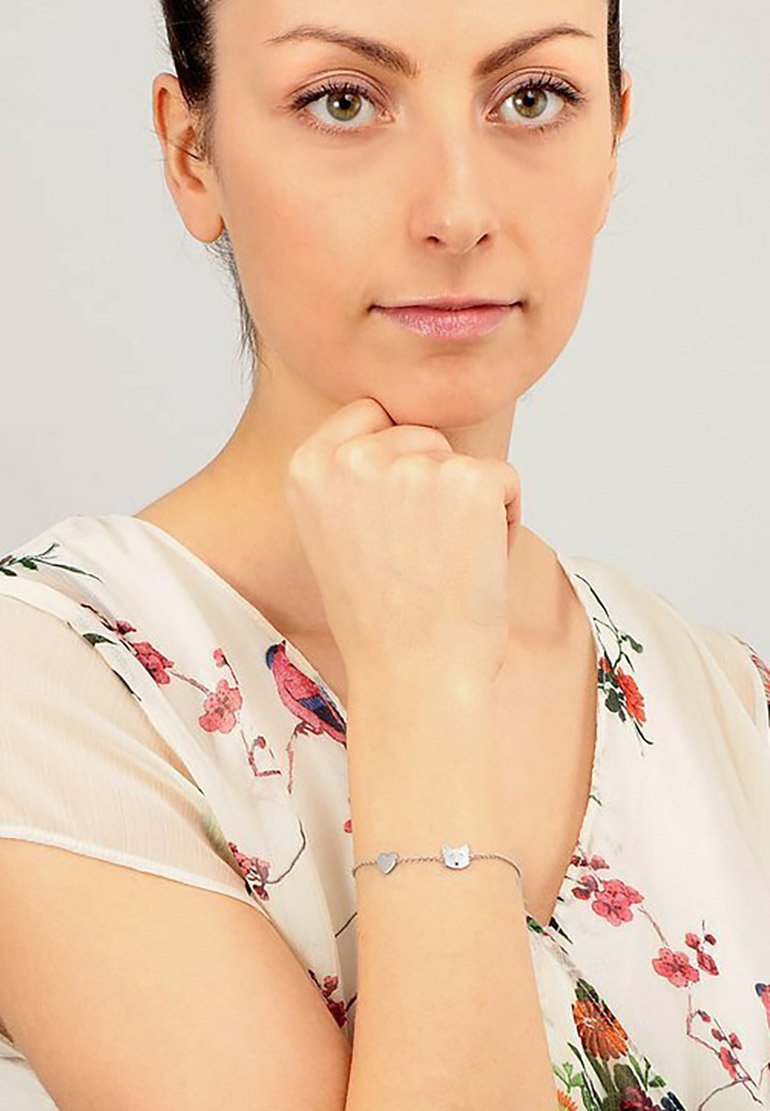 Bracciale in argento con ciondoli a forma di cuore e gatto. Il modello indossa una blusa a fiori realizzata in un tessuto morbido e trasparente.