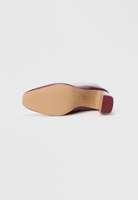 Talons en cuir bordeaux avec un bout carré, semelle texturée et un emblème doré. Fini lisse avec un talon bloc effilé pour plus de stabilité.