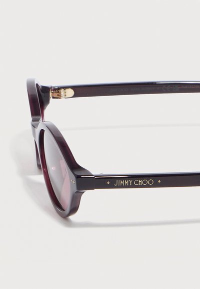 Σκούρα μωβ στρογγυλά γυαλιά ηλίου με σκουρόχρωμους φακούς και το λογότυπο "JIMMY CHOO" σε χρυσό στο πλάι του βραχίονα.
