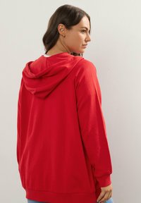 Sudadera con capucha roja, de manga larga y corte relajado. Material de algodón suave, de color sólido, con capucha ajustable y puños acanalados.