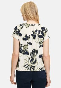 Koszula z krótkim rękawem w kremowym kolorze z ciemnozielonym i granatowym wzorem kwiatowym, z zebranym dekoltem i delikatnie elastycznym materiałem.