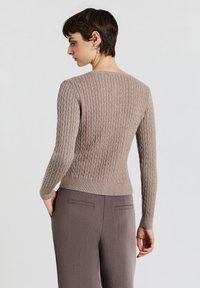 Maglione marrone chiaro lavorato a maglia con texture a coste, maniche lunghe e orlo aderente. Indossato con pantaloni abbinati a vita alta.