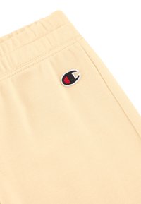 Beige katoenen sweatpants met een elastische tailleband, met een klein geborduurd logo in zwart en rood op de achterzak.
